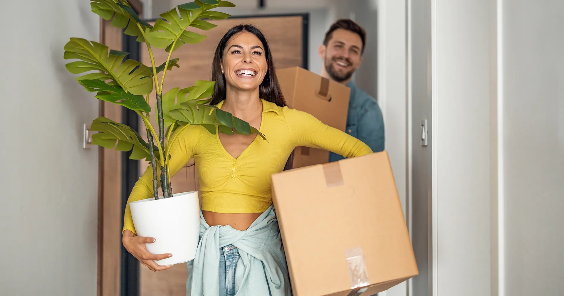 Jong stel is aan het verhuizen en hebben dozen en een plant in hun handen