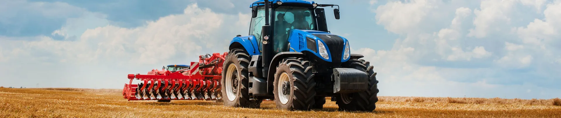 Een blauwe tractor is het land aan het omploegen met een mooie lucht op de achtergrond